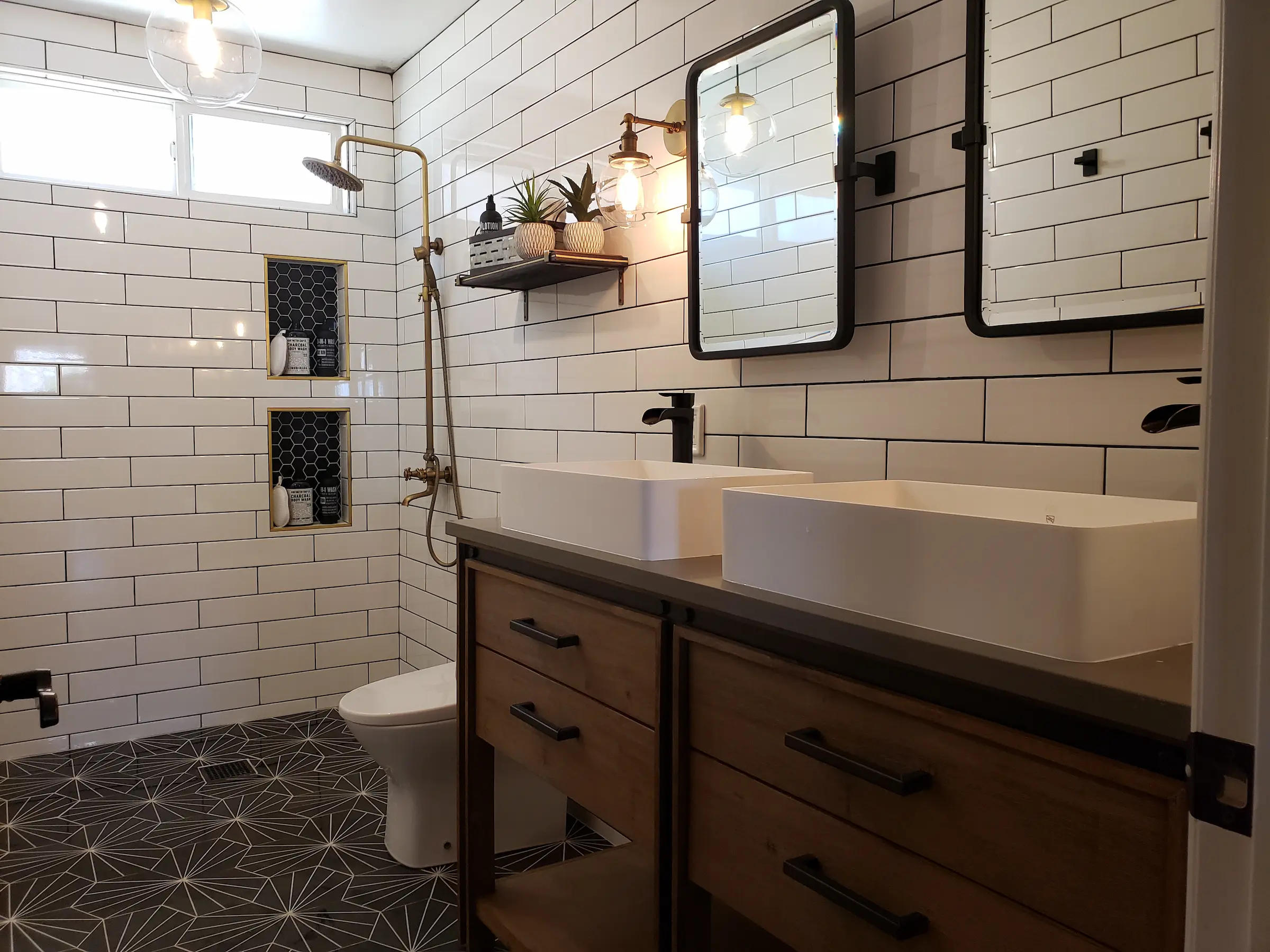 Modern bathroom with dual sinks, wooden cabinetry, and geometric tiled floor.
