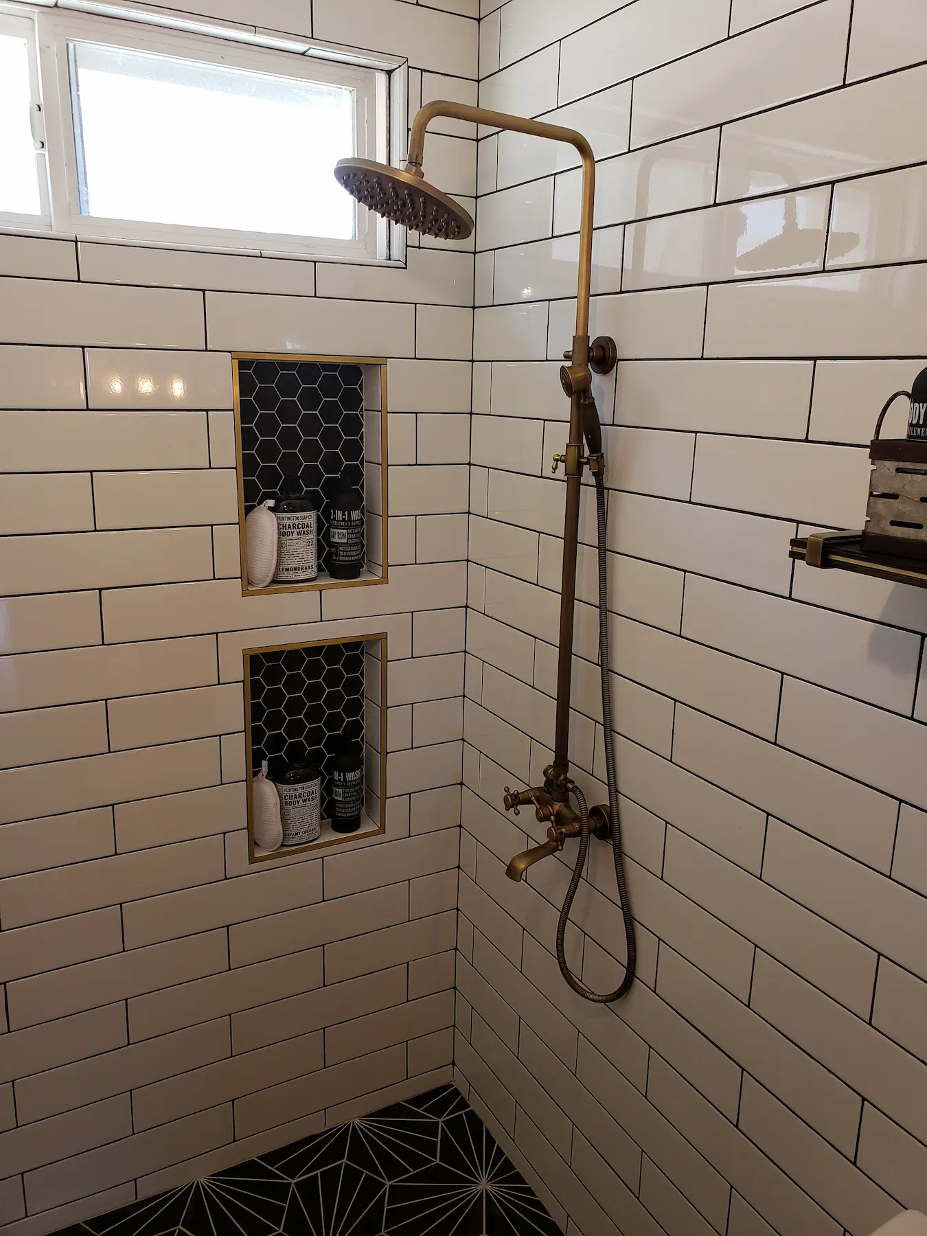 Modern shower with brass fixtures and black hexagonal tile niches.