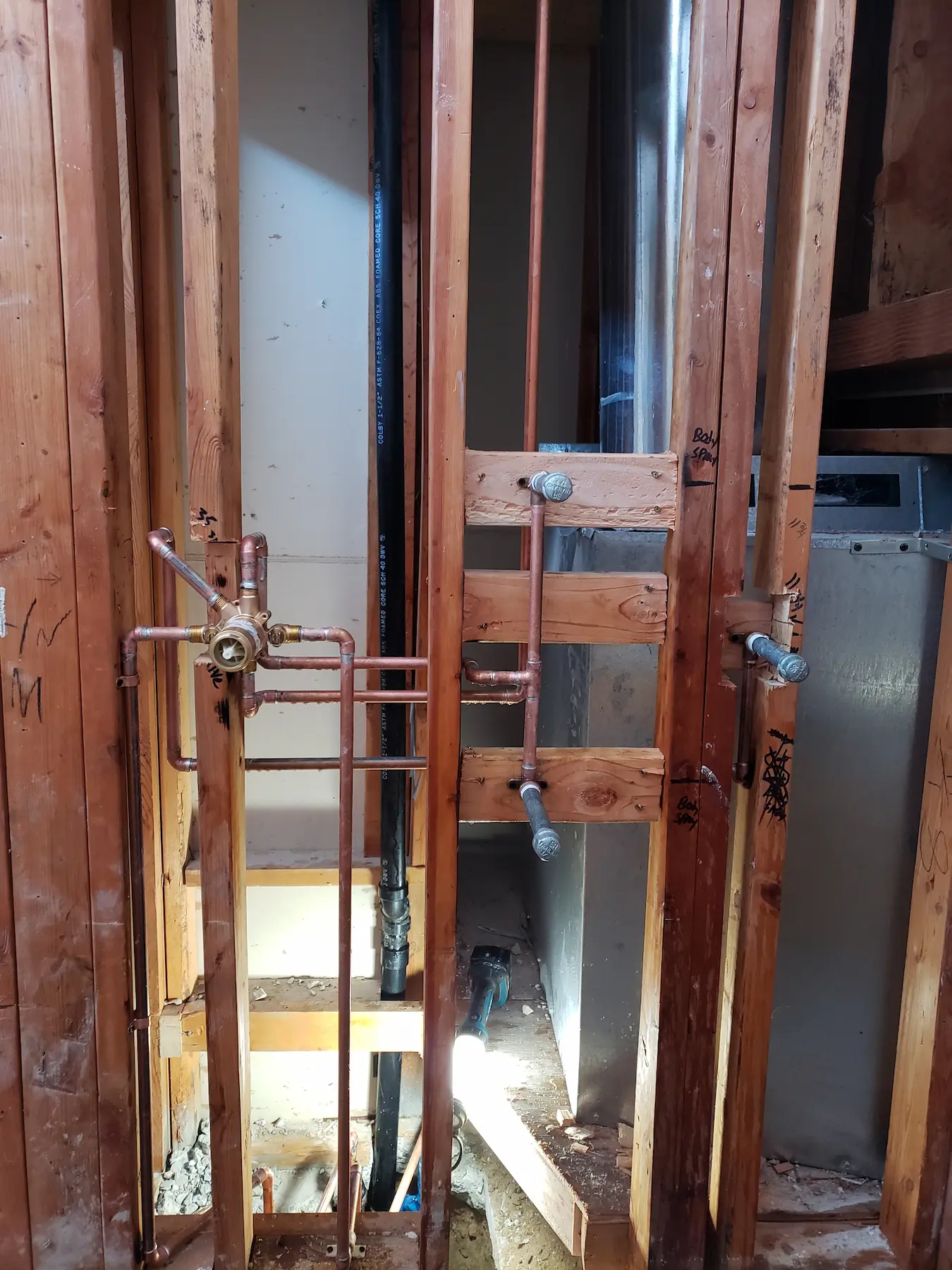Exposed wooden framing with copper plumbing pipes in a construction site.