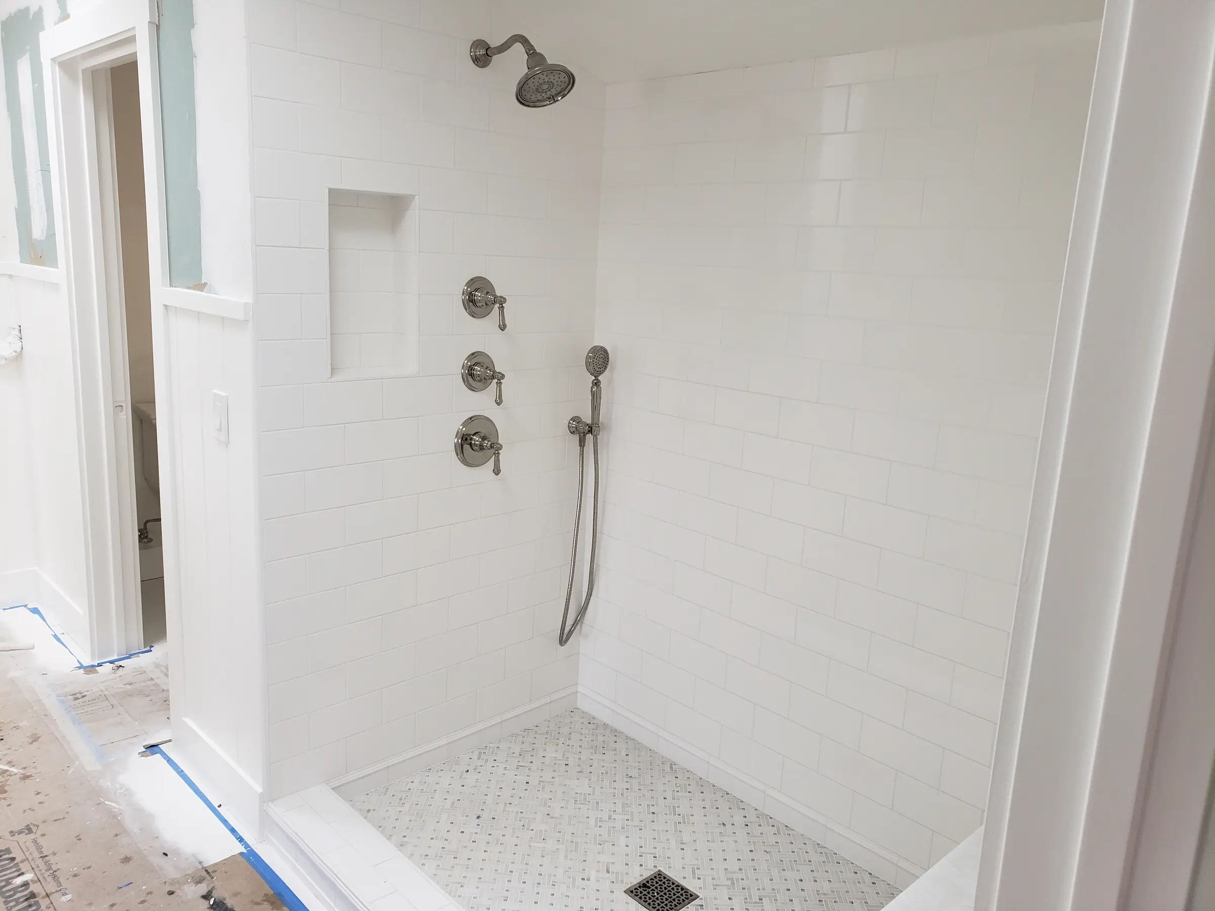 Newly tiled white shower with silver fixtures in a bathroom under renovation.