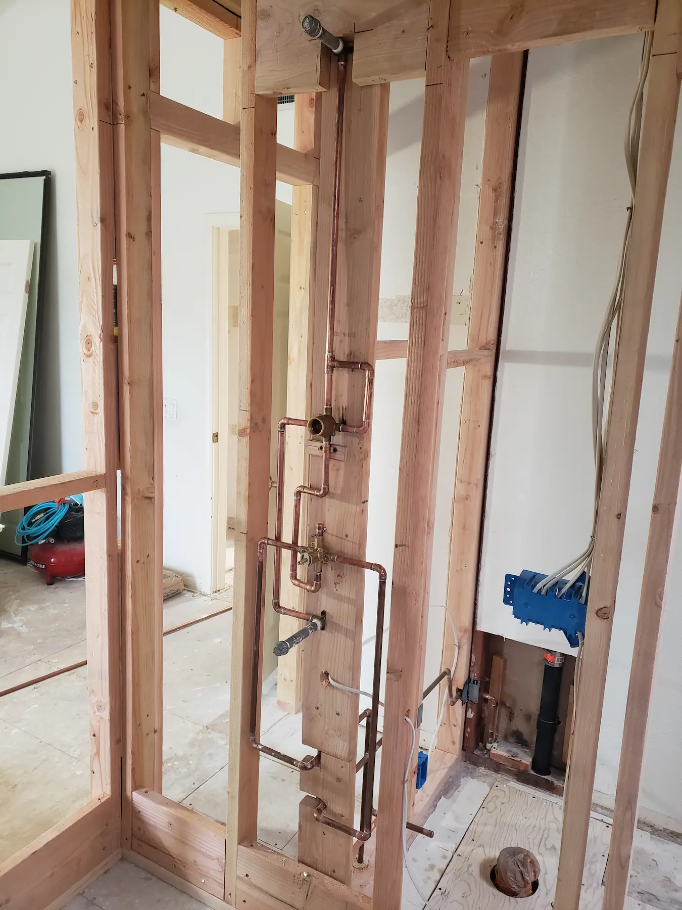 Exposed wooden framing with copper plumbing and electrical wiring in a room under construction.