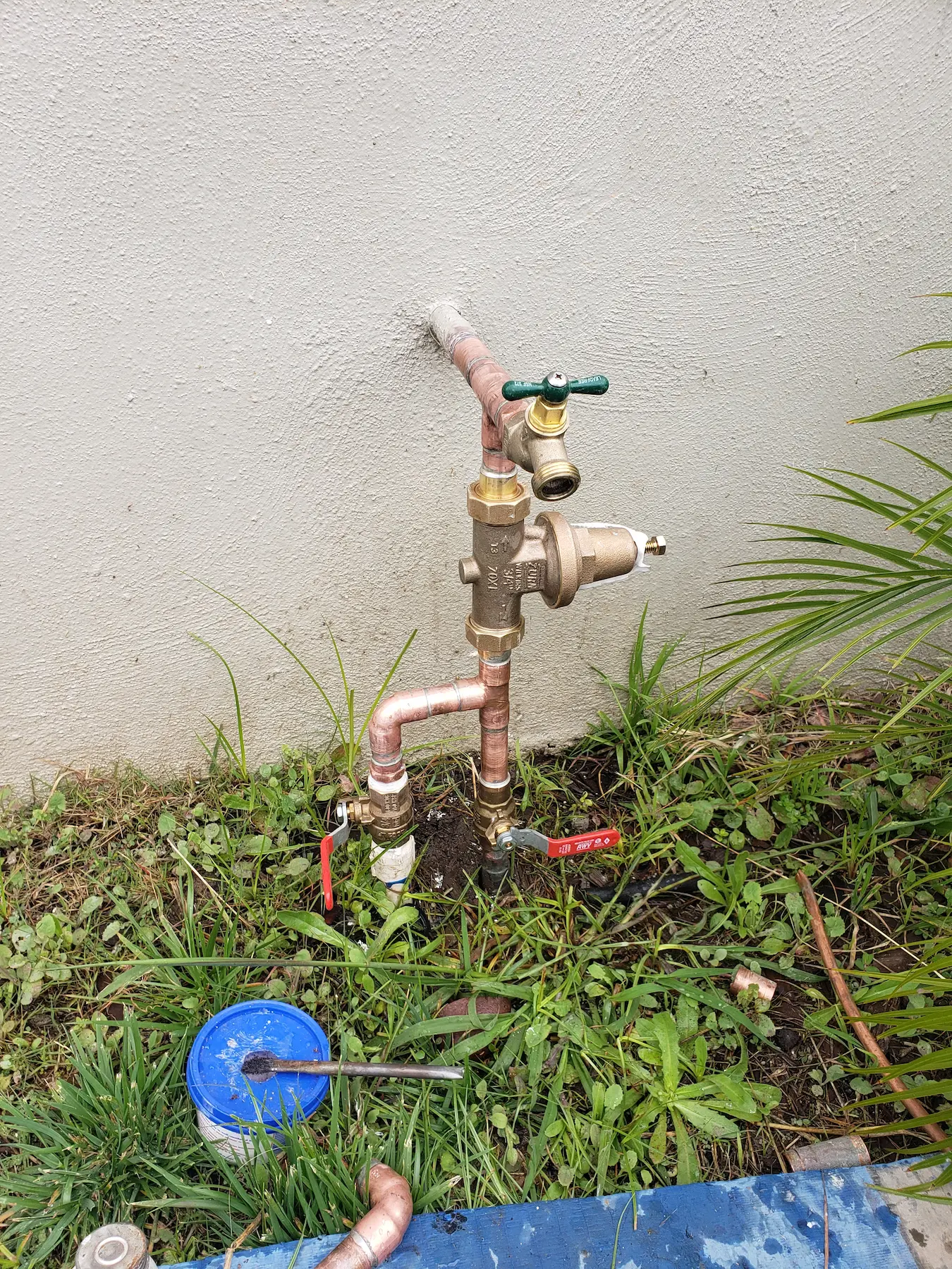 Copper outdoor water faucet setup with valves and pressure regulator.