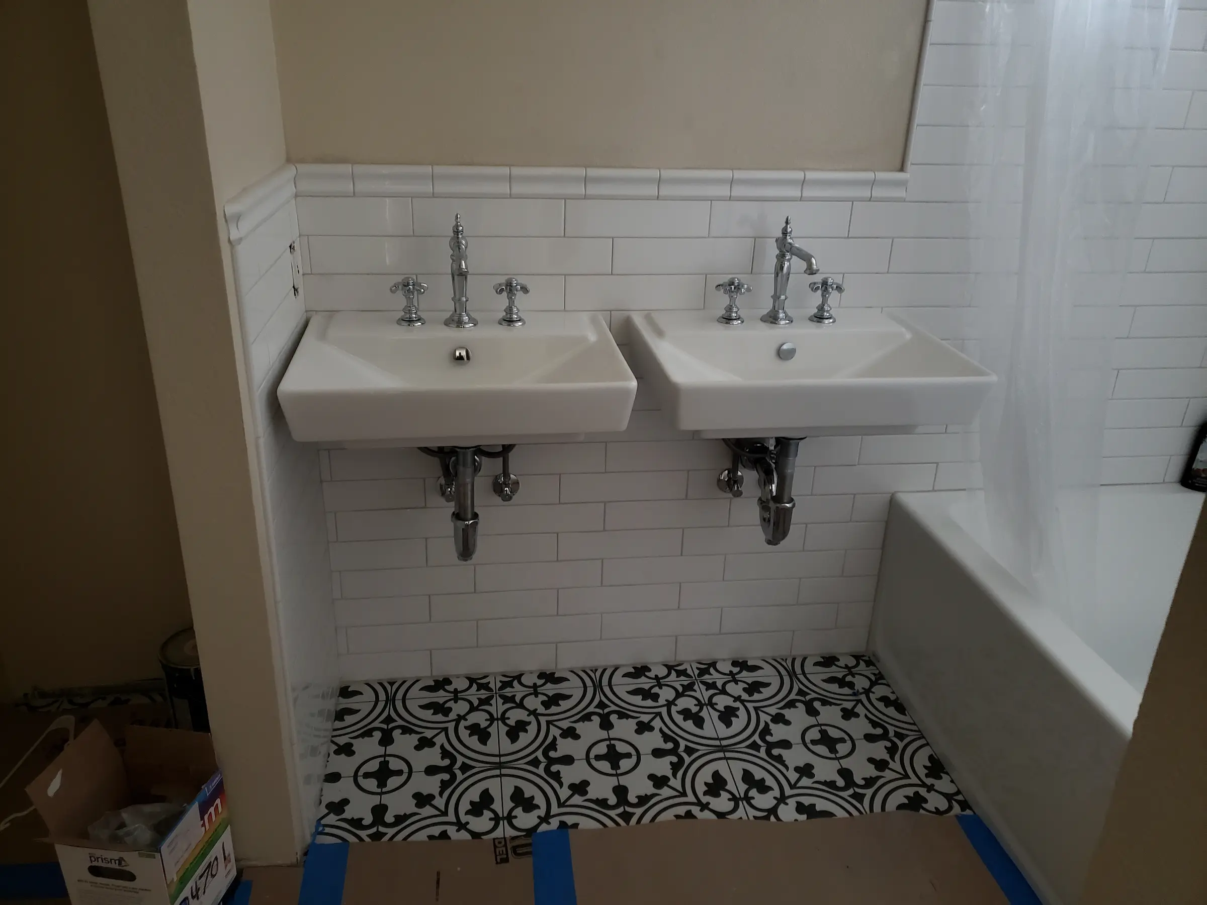 Two white sinks with chrome faucets over patterned black and white tile floor in a bathroom.