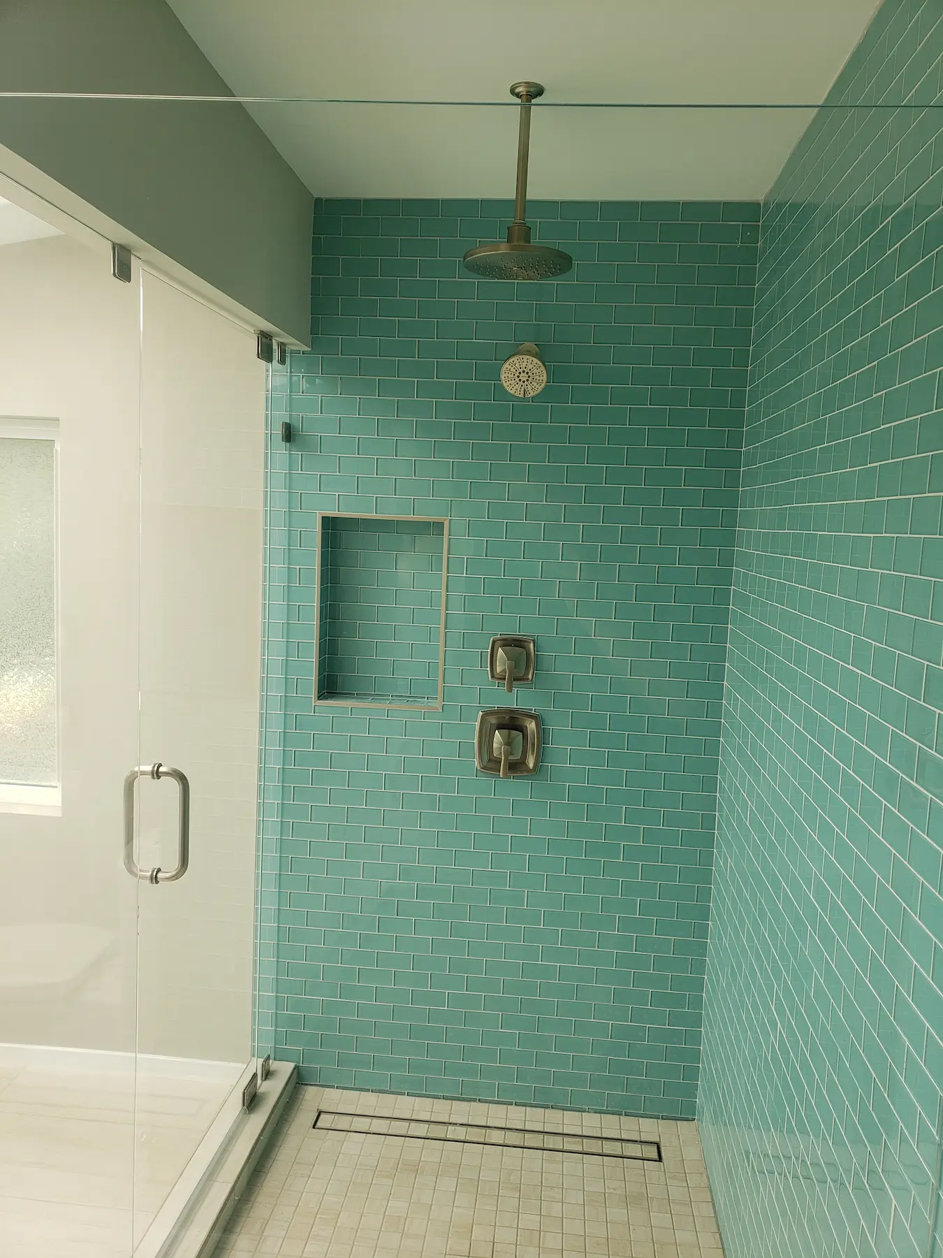 Modern shower with teal subway tiles and glass door.
