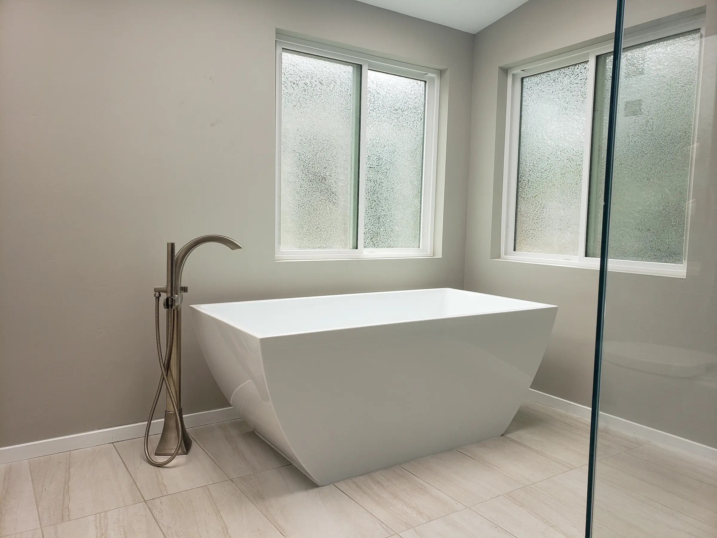 Modern white freestanding bathtub with sleek faucet and frosted windows.