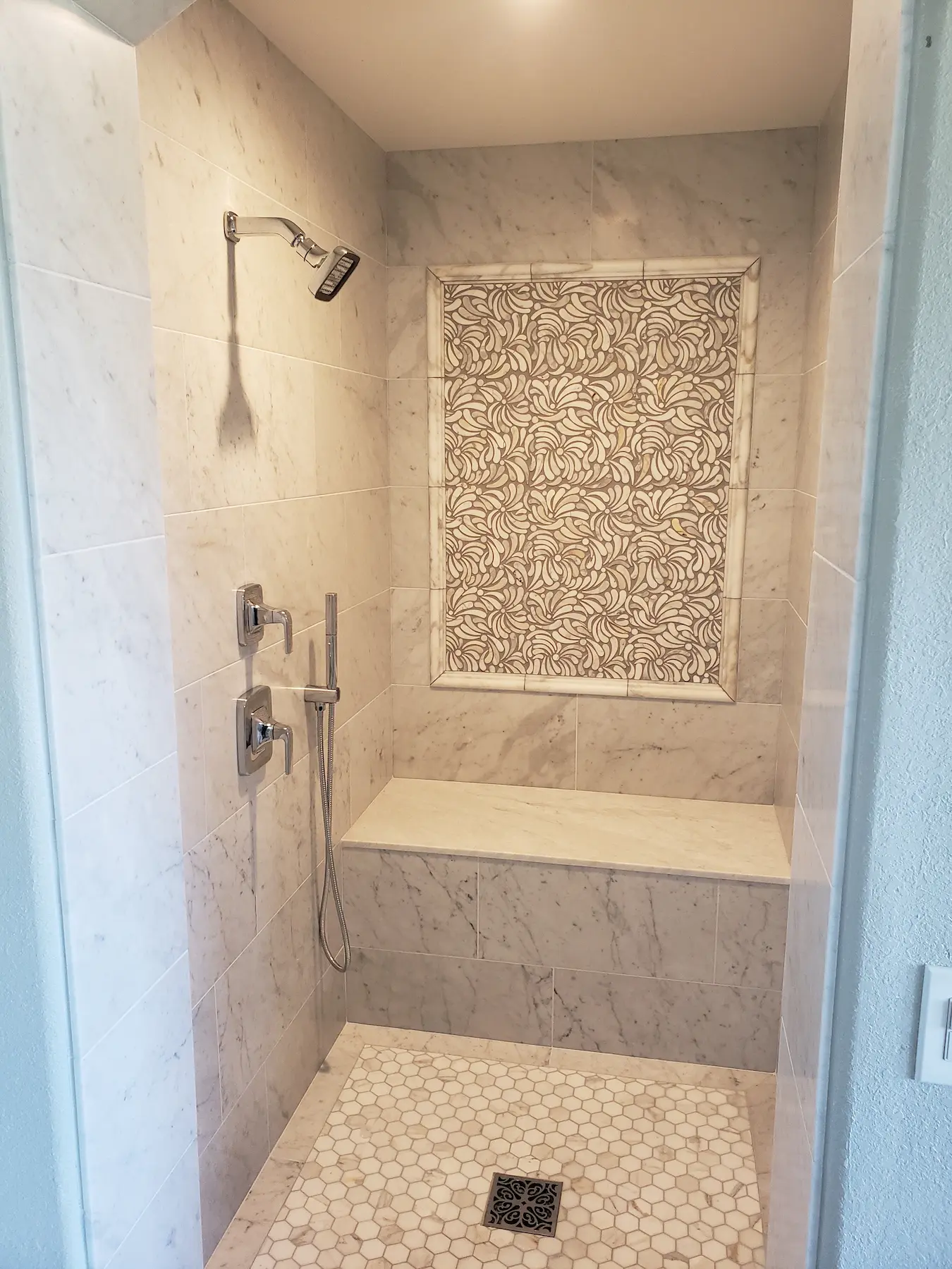 Modern marble shower with patterned accent tile and built-in bench.