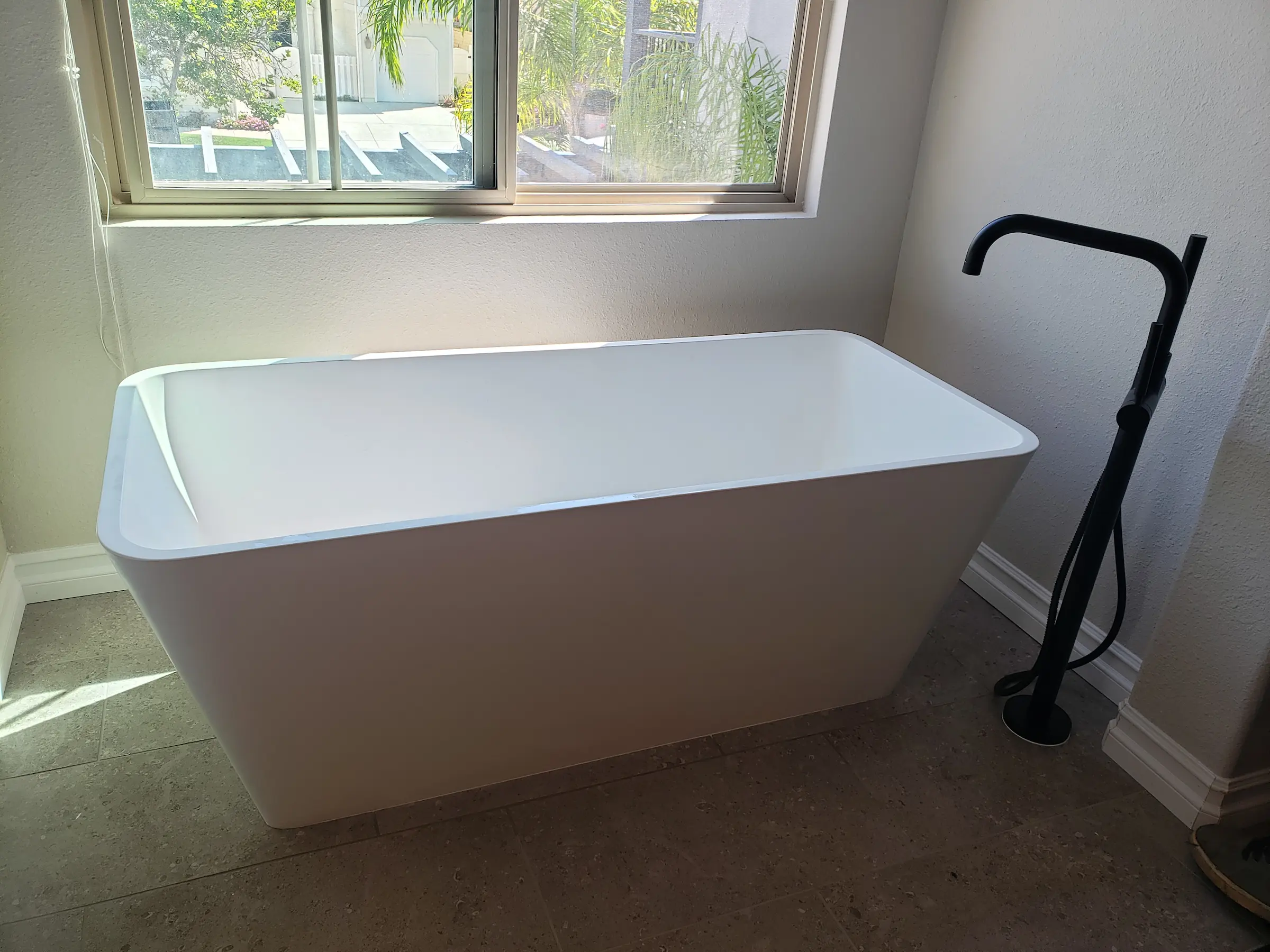 Modern white freestanding bathtub with a black floor-mounted faucet.