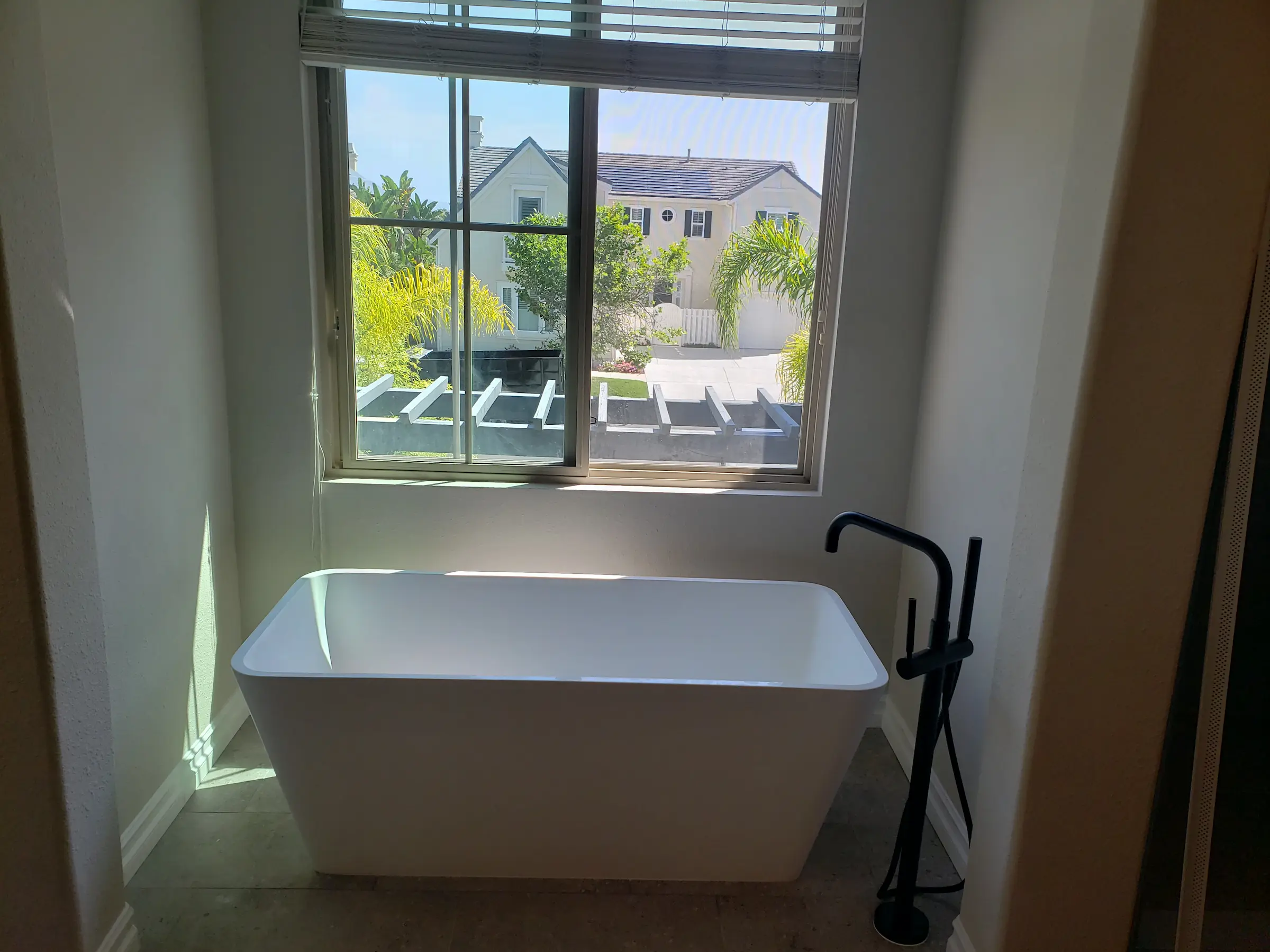 Modern white bathtub with black faucet near a sunny window.