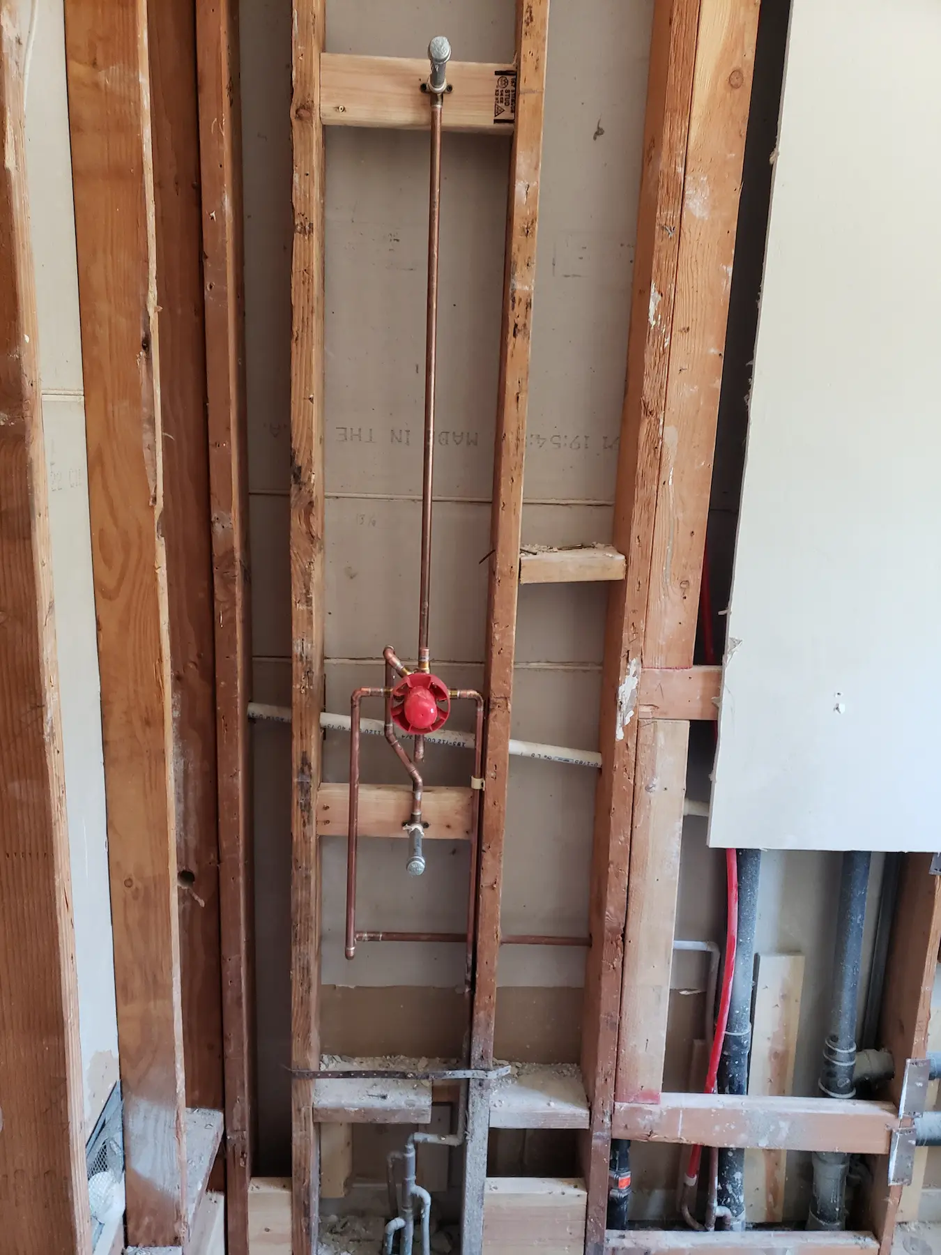 Exposed wall framing with copper plumbing and a red valve handle.